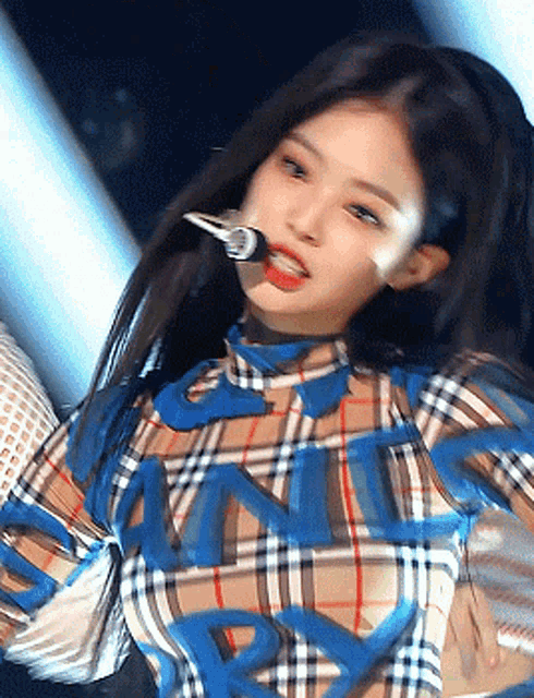 a woman is singing into a microphone while wearing a plaid shirt with the word burberry on it .