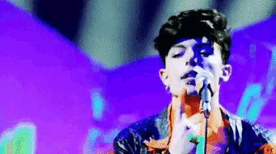 a man is singing into a microphone with a purple background behind him .