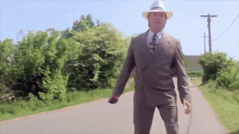 a man in a suit and hat is walking down the road