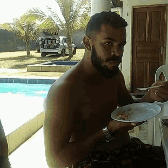 a shirtless man with a beard is eating from a plate