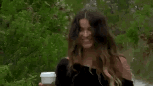 a woman is laughing while holding a cup of coffee and scratching her head .