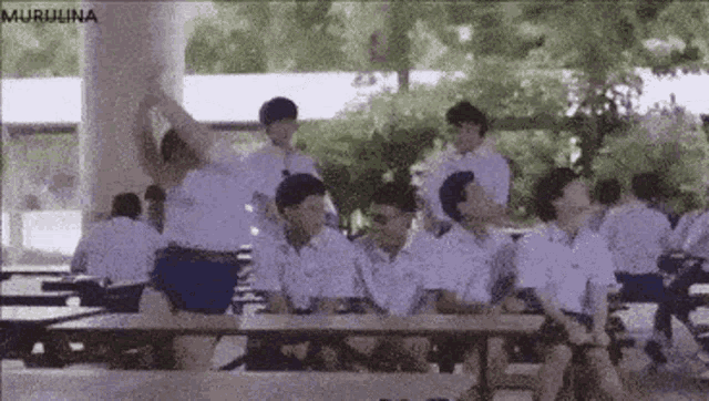 a group of young men in school uniforms are sitting at tables in a cafeteria .