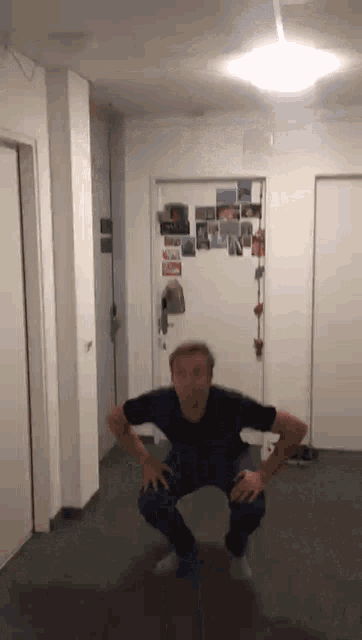 a man squatting down in a hallway with a door behind him