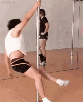 a man is doing a pole dance in front of a mirror while a woman watches .