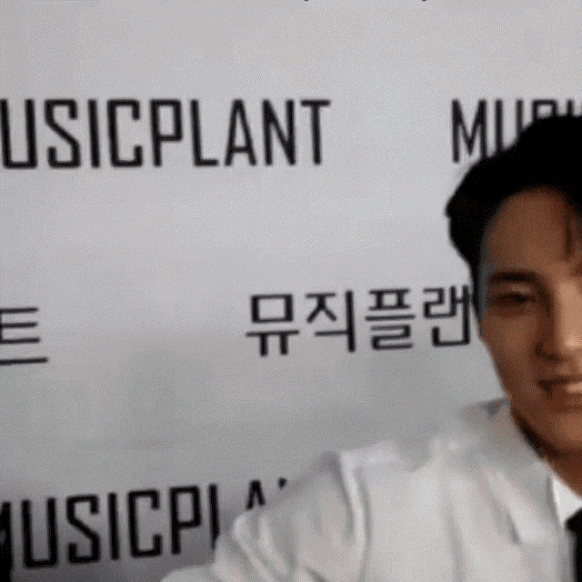 a man in a white shirt and tie stands in front of a music plant sign