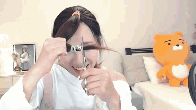 a woman is cutting her hair with scissors in front of a stuffed bear