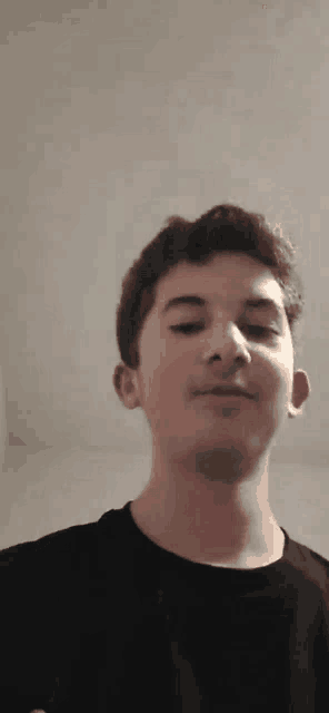 a young man in a black shirt is looking at the camera and smiling .