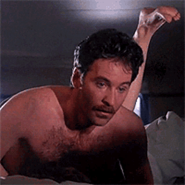 a shirtless man with a mustache is laying on a bed with his feet up