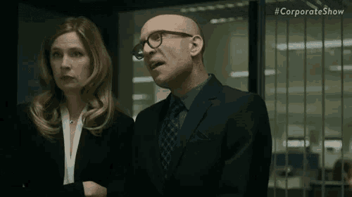 a man in a suit and tie is standing next to a woman in a suit and glasses .