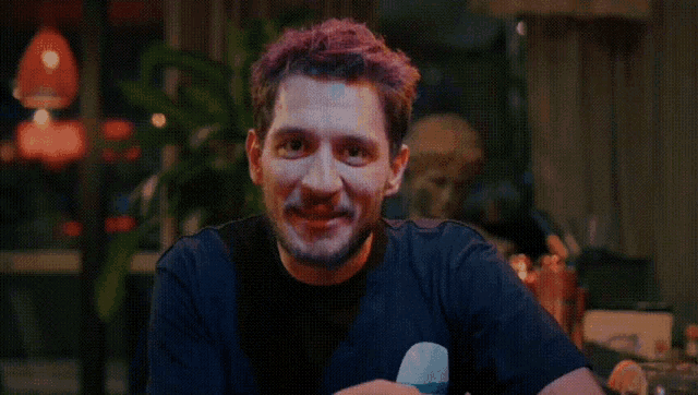 a man with purple hair and a black shirt smiles at the camera