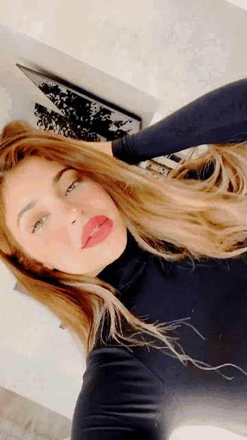 a woman wearing a black turtleneck and red lipstick takes a selfie