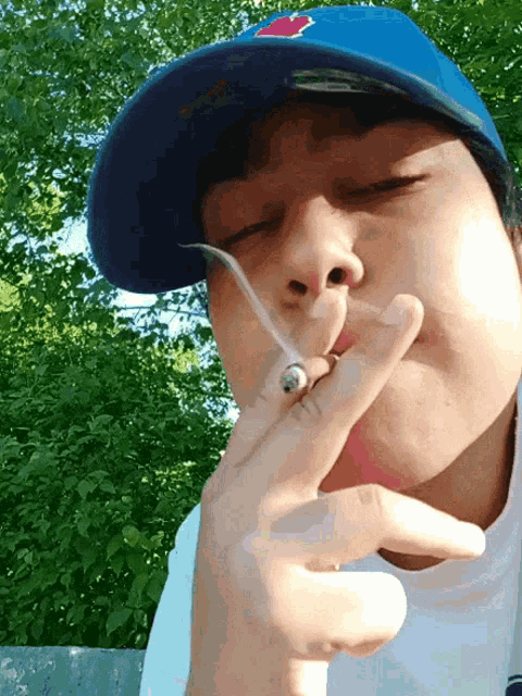 a boy wearing a blue hat is smoking a cigarette outside