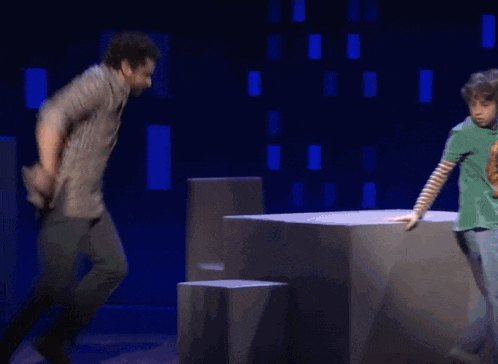 a boy in a green shirt is standing next to a man in a brown shirt on a stage