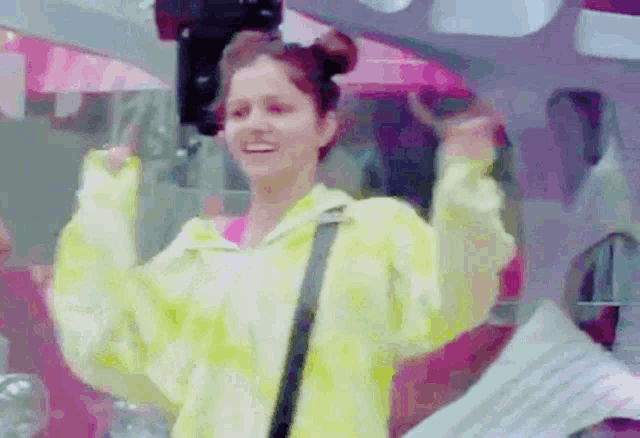 a woman in a yellow jacket is dancing in a room with her arms in the air .