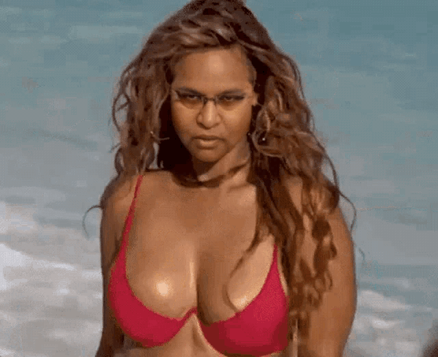 a woman in a red bikini and glasses is standing on the beach
