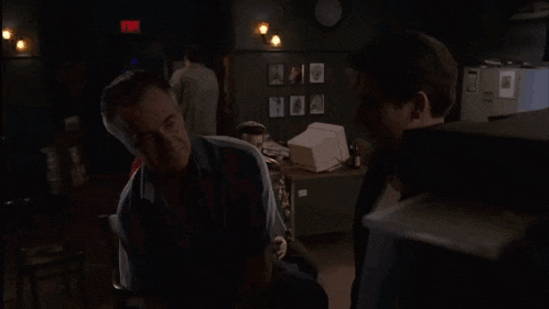 two men are standing in a dark room with a red exit sign in the background