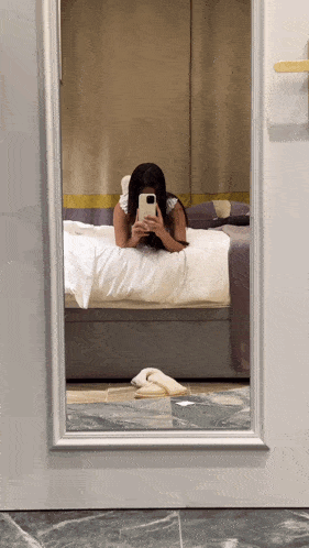 a woman laying on a bed taking a selfie in a mirror