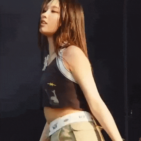 a woman in a black crop top and khaki pants is holding a microphone and dancing on a stage .
