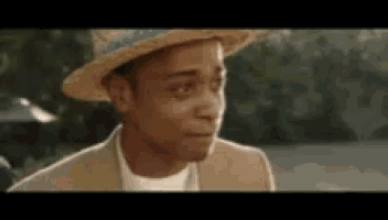 a man wearing a hat and a suit is looking at the camera .