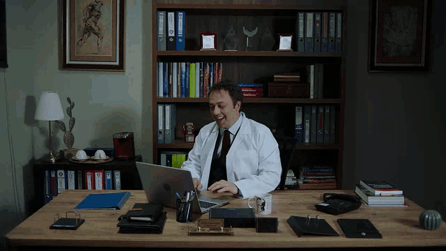 a man in a lab coat sits at a desk with a laptop and a mug that says ' istanbul ' on it