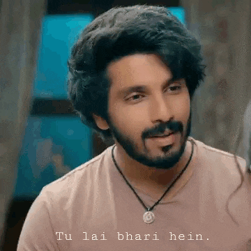 a man with a beard wearing a necklace and a pink shirt is talking .