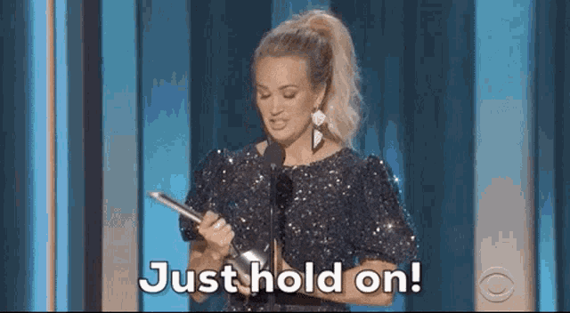country pop artist is holding a microphone and giving a speech on stage at awards .