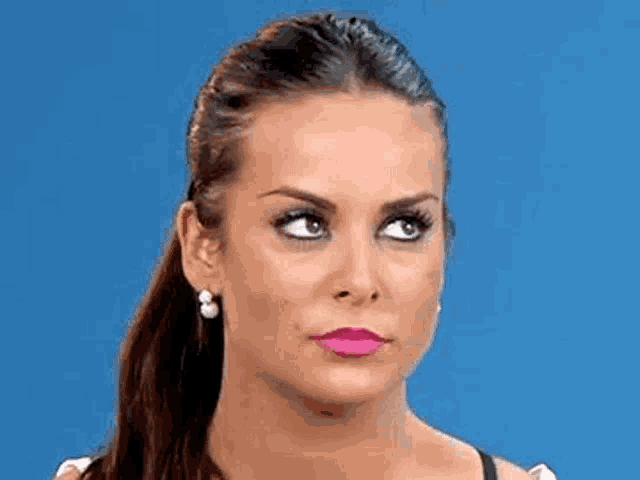 a close up of a woman 's face with a blue background . she is wearing pink lipstick and earrings .