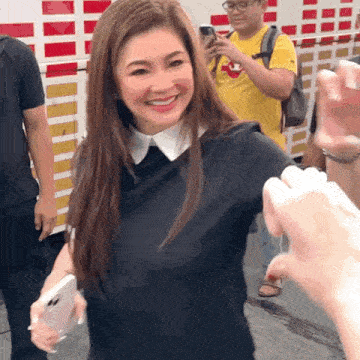 a woman in a black shirt with a white collar smiles while holding a cell phone