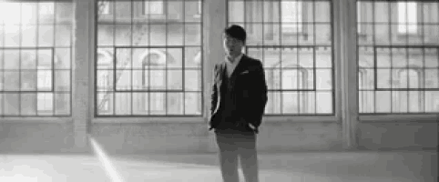 a man in a suit and tie is standing in front of a large window in a black and white photo .