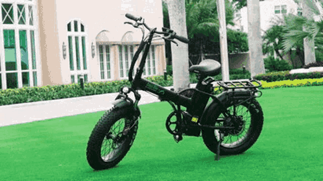 a black folding electric bike is parked on a lush green field .