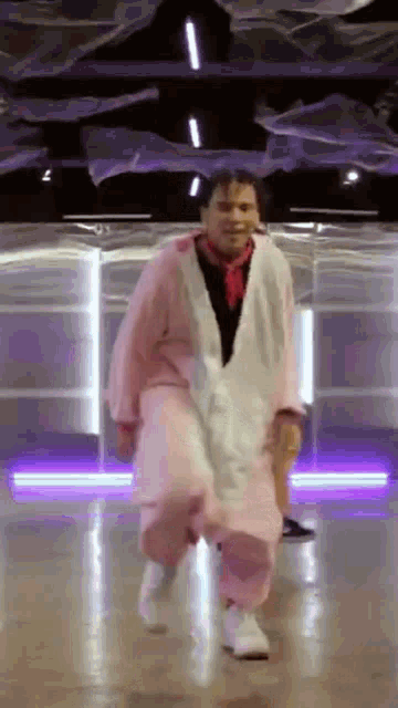 a man in a pink and white outfit is dancing on a dance floor in a room .