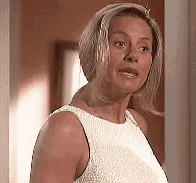 a woman in a white dress is making a funny face while standing in a hallway .