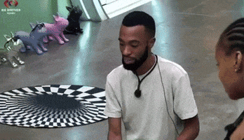 a man with a beard is sitting in front of a checkered rug and talking to a woman .