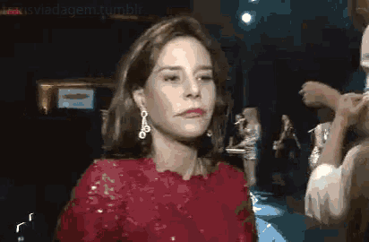 a woman wearing a red dress and earrings is standing in front of a crowd .