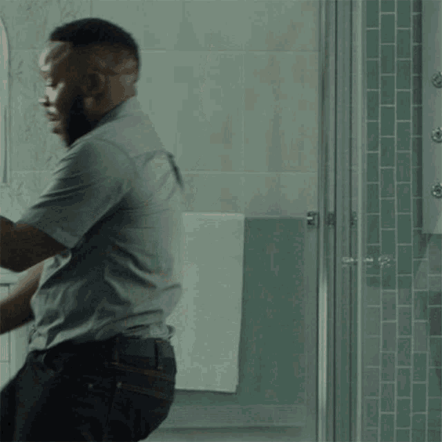 a man in a grey shirt is standing in front of a bathroom mirror
