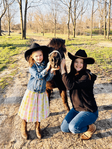two young girls in cowboy hats are holding a small horse