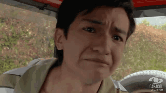 a young man is making a funny face in a car with caracol television in the background .