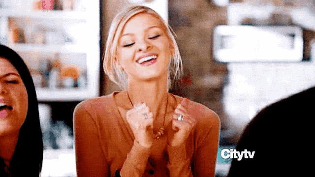 a woman is laughing while sitting at a table with her hands in her pockets .