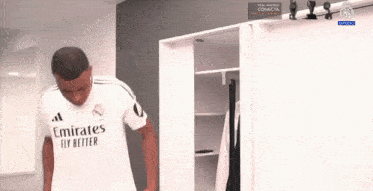 a man wearing a white emirates fly better shirt is standing in a locker room .