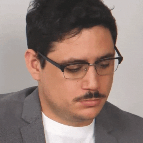 a man with glasses and a mustache looks down at something