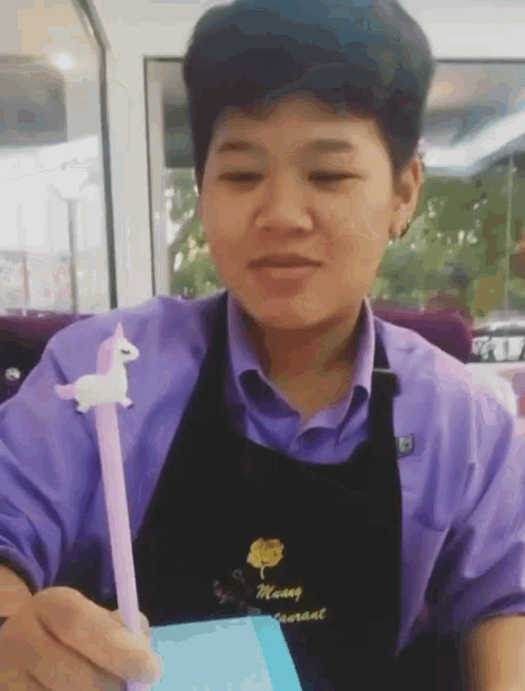 a man wearing a purple shirt and black apron is holding a unicorn pen