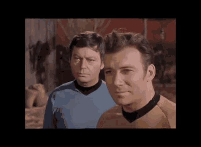 two men are standing next to each other and looking at the camera . one of the men is wearing a yellow shirt .