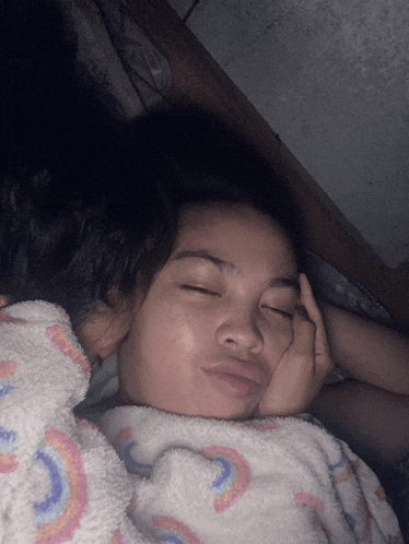 a girl with her eyes closed is wrapped in a blanket with a rainbow pattern