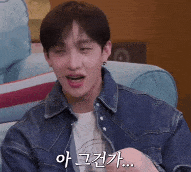 a man wearing a denim jacket is sitting on a couch with a foreign language written on his face