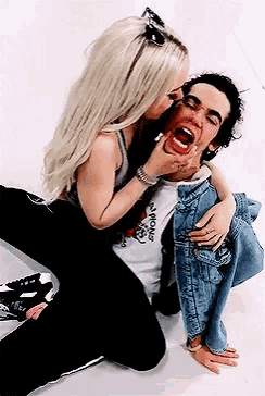 a woman is kissing a man on the cheek while he is laying on the floor