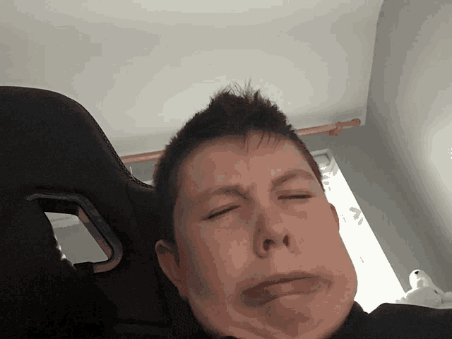 a young boy sitting in a chair with his eyes closed making a funny face