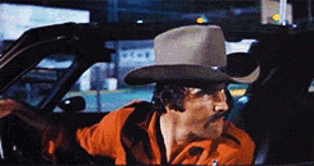 a man wearing a cowboy hat and mustache is driving a car