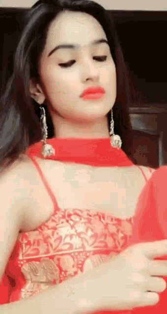 a woman in a red top and gold earring looks at the camera