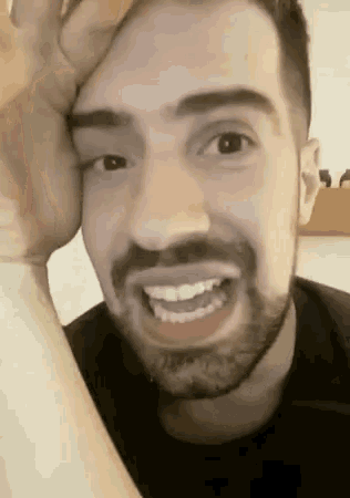 a man with a beard is smiling with his hand on his head