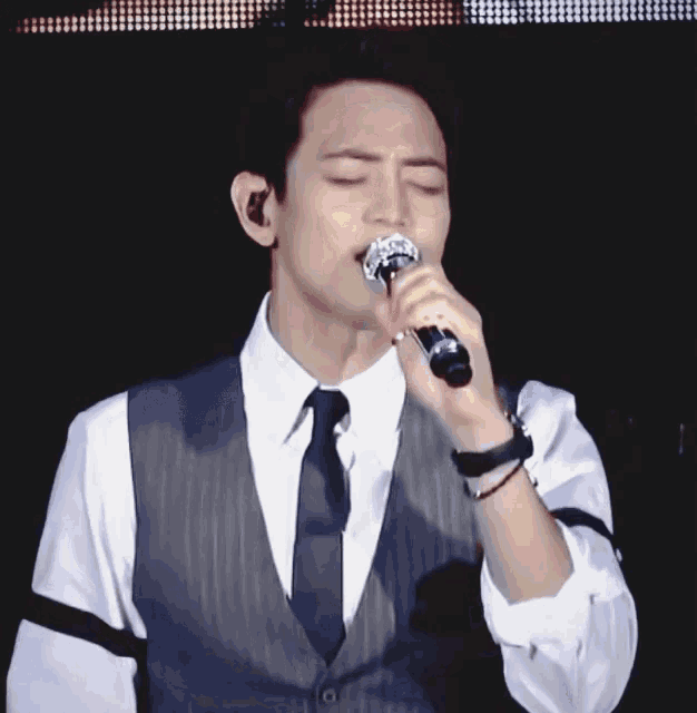 a man singing into a microphone while wearing a vest and tie